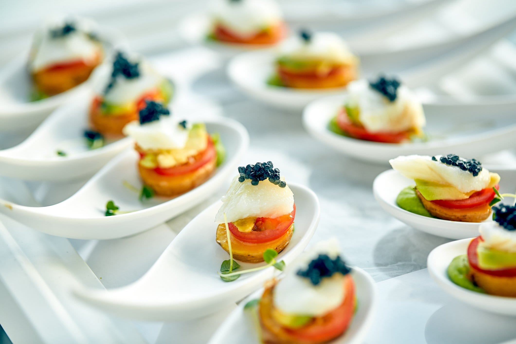 Canapés on white spoons topped with caviar, tomato and avocado