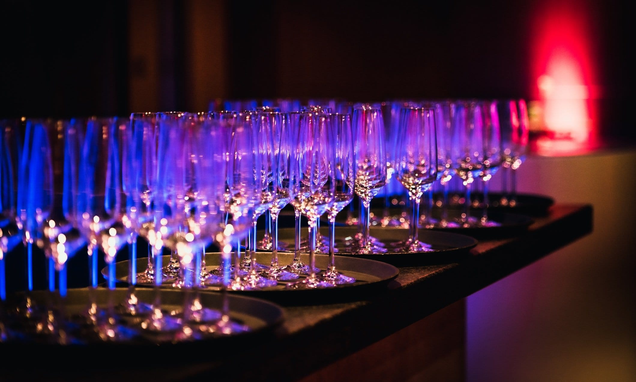 Champagne and wine glasses on trays under blue and pink event lighting
