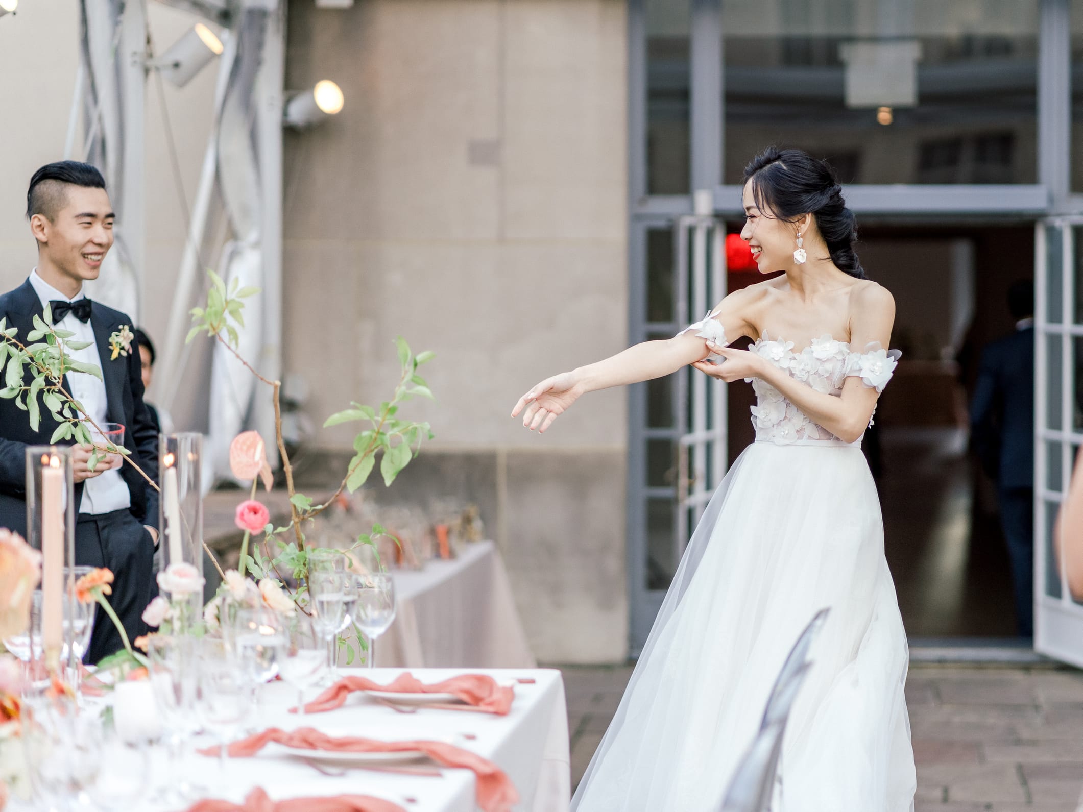 Outdoor wedding reception with long tables, ghost chairs, and coral florals in a NYC garden